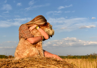 A girl with long blonde hair hugging a shaggy dog on a bright sky background nature