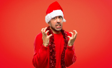 Man with red clothes celebrating the Christmas holidays annoyed angry in furious gesture on red background