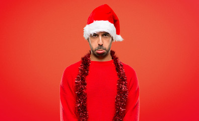 Man with red clothes celebrating the Christmas holidays with sad and depressed expression on red...
