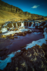 The Noname waterfall with golden clouds in the sky. The flowing water is captured by a long exposure. Amazing blue color of water from the glacier. Natural and colorful environment...