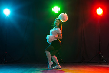 Cheerleading young woman dancing with pom-poms on colourful background © satura_
