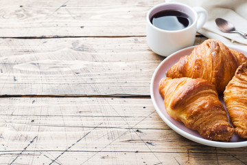 Breakfast croissants on a plate and a Cup of coffee, wooden background, copy space.