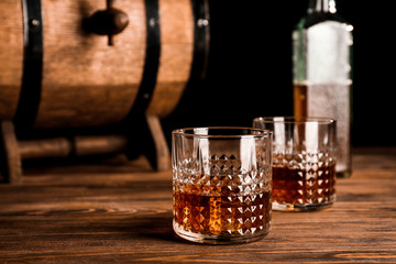 Glasses of whiskey near barrel on wooden table