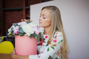Happy blonde woman in a modern office with flowers in a hat box. Bouquet of peonies.