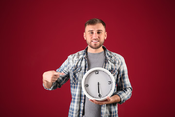 Young man with clock on color background