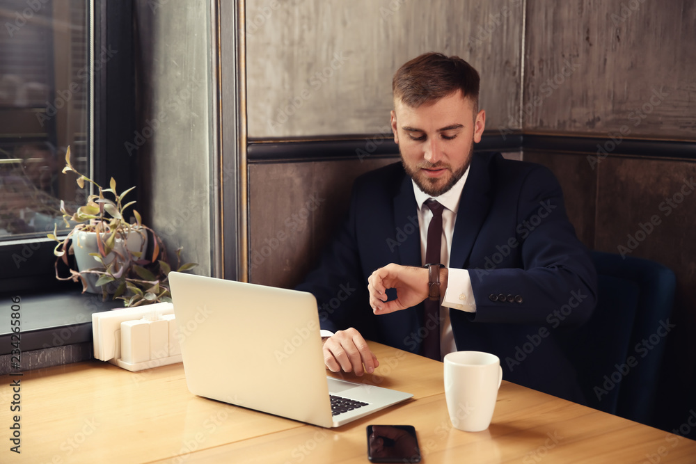 Wall mural businessman looking at his watch while working in cafe