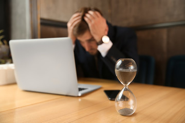 Hourglass on table of troubled businessman sitting in cafe