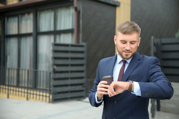 Businessman with cup of coffee looking at his watch outdoors