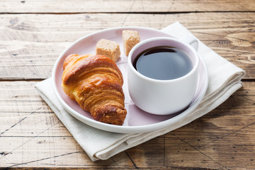 Breakfast croissants on a plate and a Cup of coffee, wooden background, copy space.