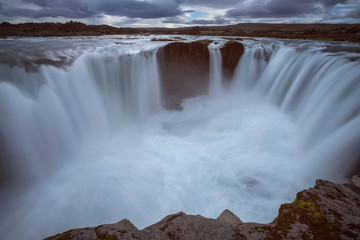 The Hrafnabjargarfoss Waterfall with golden clouds in the sky. The flowing water is captured by a long exposure. Amazing blue color of water from the glacier. Natural and colorful environment.