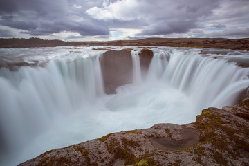The Hrafnabjargarfoss Waterfall with golden clouds in the sky. The flowing water is captured by a...