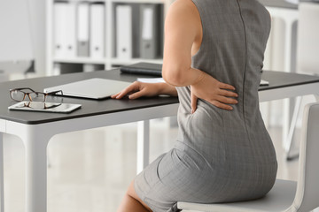 Young woman suffering from back pain in office