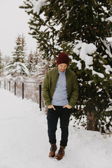 Young Trendy Man in Green Bomber Jacket Enjoying the Winter Snow on a Small Bridge in Colorado