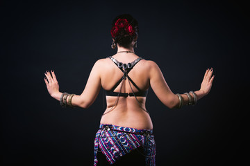 Women performs belly dance in ethnic dress on black background