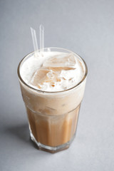 Glass of cold coffee with milk and ice cubes on light background