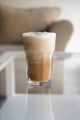 Glass of cold coffee with milk and ice cubes on table