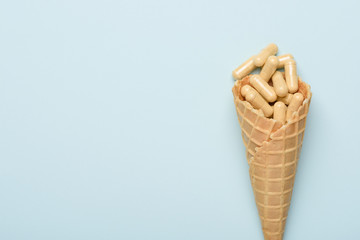 Pills in ice cream waffer cone medicine concept on blue background with copy space