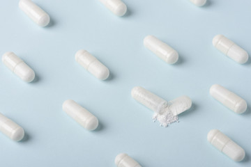 Pills pattern with one capsule open and white powder spilling over blue background