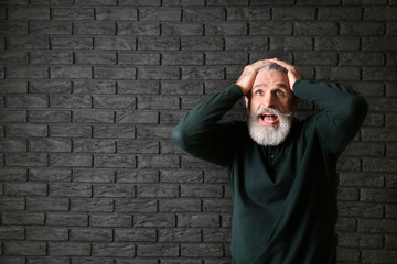 Emotional senior man after making mistake on dark background