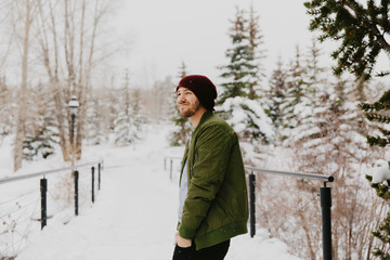 Fototapeta na wymiar Young Trendy Man in Green Bomber Jacket Enjoying the Winter Snow on a Small Bridge in Colorado
