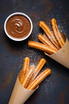 Fried traditional churro sticks with sugar powder cinnamon and bowl of chocolate dip on dark table top view
