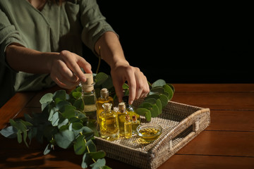 Woman taking bottles of eucalyptus essential oil from tray on table