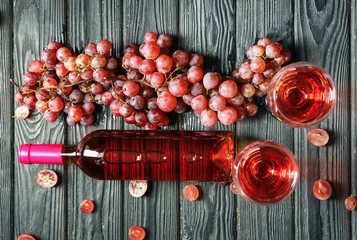 Bottle, glasses of tasty wine and grapes on wooden table