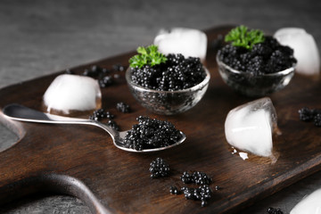 Fototapeta na wymiar Spoon and bowls with delicious black caviar on wooden board