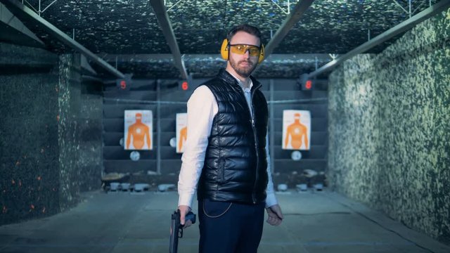 A man holds a gun and looks at a camera, close up.