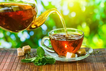 Cercles muraux Theé L& 39 heure du thé. Verser du thé chaud dans une tasse. Fond de nature verdoyante.