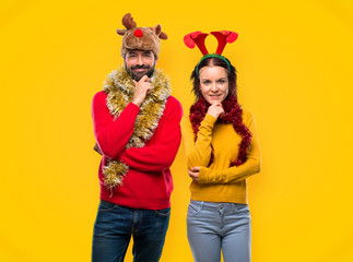 Couple dressed up for the christmas holidays smiling and looking to the front with confident face on yellow background