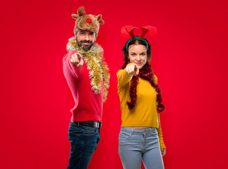 Couple dressed up for the christmas holidays points finger at you with a confident expression on isolated red background