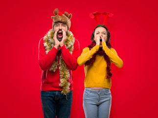Couple dressed up for the christmas holidays shouting with mouth wide open and announcing something on isolated red background