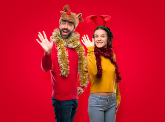 Couple dressed up for the christmas holidays saluting with hand with happy expression on isolated red background