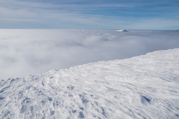 Mountain tops covered with snow above the white heavy clouds.
