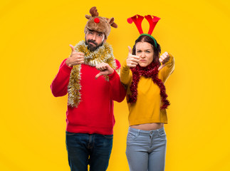 Couple dressed up for the christmas holidays making good-bad sign. Undecided between yes or not on yellow background