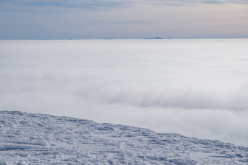 Obraz premium Mountain tops covered with snow above the white heavy clouds.