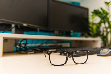 desktop in the light office on the table are two monitors, a laptop, glasses, headphones, a keyboard, a mouse, a mug, a notebook and a handle at the table office chair