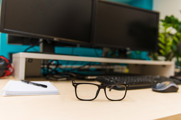 desktop in the light office on the table are two monitors, a laptop, glasses, headphones, a keyboard, a mouse, a mug, a notebook and a handle at the table office chair