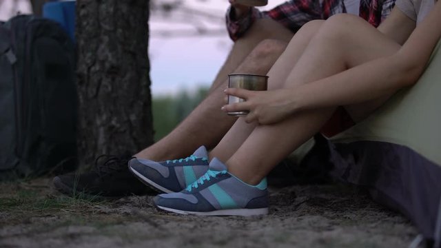 Hikers in sport shoes sitting in tent, drinking tea, resting after busy day