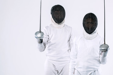 Two Young fencers athletes wearing mask and white fencing costume and holding the sword. Isolated...