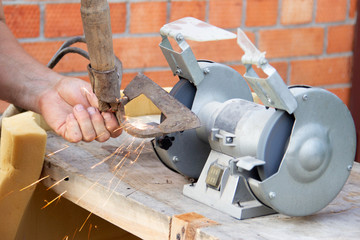 mans hand sharpens a hoe on electric grindstone in rural shed