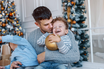 A daddy with his two sons twins in front of the christmas tree  with candles and gifts hugging and having fun. New year's eve. Cozy holiday at the fir-tree. love, happiness and big family concept