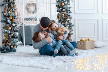 A a daddy with his two sons twins in front of the christmas tree  with candles and gifts hugging and having fun. New year's eve. Cozy holiday at the fir-tree. love, happiness and big family concept