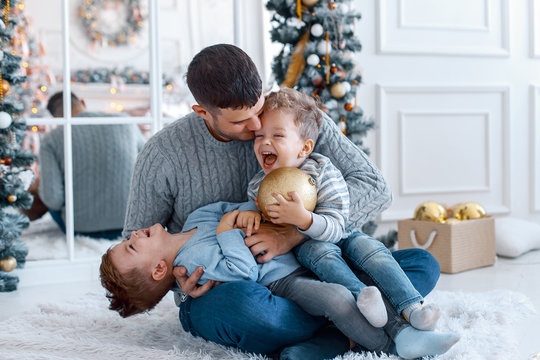 A a daddy with his two sons twins in front of the christmas tree  with candles and gifts hugging and having fun. New year's eve. Cozy holiday at the fir-tree. love, happiness and big family concept
