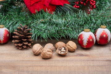 Winter holiday decoration: Blooming Red Poinsettia, Pine, Berry bush, Christmas tree balls, pine cone, walnuts and green garland on wooden background.