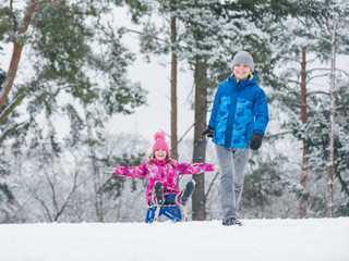 Fototapeta na wymiar Happy boy and girl riding sled and having fun. Children play outdoors in snow - sledding. Kids sled in snowy park in winter. Outdoor fun for family Christmas vacation.