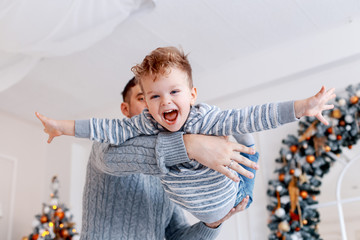 A daddy with his two sons twins in front of the christmas tree  with candles and gifts hugging and having fun. New year's eve. Cozy holiday at the fir-tree. love, happiness and big family concept