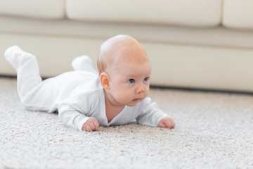 Childhood, babyhood and people concept - little baby boy or girl crawling on floor at home