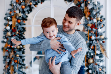 A daddy with his two sons twins in front of the christmas tree  with candles and gifts hugging and having fun. New year's eve. Cozy holiday at the fir-tree. love, happiness and big family concept